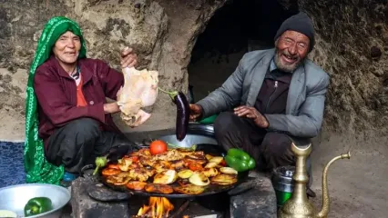 (ویدئو) پخت نان، مرغ، سیب زمینی و بادمجان روی ساج توسط یک زوج غارنشین افغان